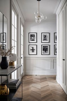 a hallway with pictures on the wall and a table in front of it, along with two vases filled with flowers