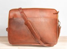 a brown leather messenger bag sitting on top of a wooden table next to a white wall