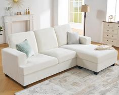 a living room with a white sectional couch and pillows on the floor next to a rug