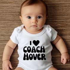 a baby sitting on the floor wearing a white bodysuit that says i love coach hover