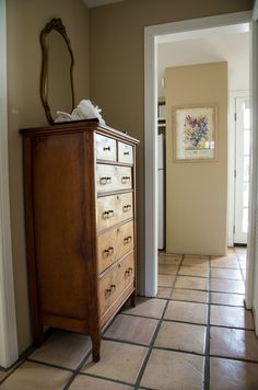 an empty room with a dresser, mirror and door leading to another room in the background