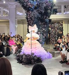 a woman in a pink and purple dress standing on a stage with people watching her