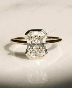 an engagement ring with a cushion cut diamond in the center, on a white surface