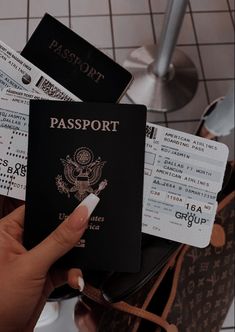 a person holding up a passport and some other items in front of them on a tiled floor