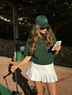 a woman in a green shirt and white skirt holding a cell phone