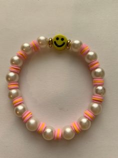 Smiles and pearls is an stretchy bracelet featuring a cute yellow smiley face with white pearls and some pink and orange clay beads. Trendy White Pearl Bracelet With Pearl Charm, Cute White Pearl Bracelet With Colorful Beads, Cute White Pearl Bracelet, Trendy White Beaded Bracelet With Pearl Charm, Trendy Pink Pearl Bracelet With Letter Beads, Cute White Beaded Pearl Bracelet, Pink Smiley Face Round Bead Jewelry, Pink Smiley Face Round Beaded Jewelry, Cheerful White Bracelets With Colorful Beads