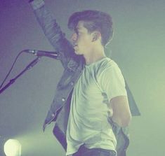 a young man standing in front of a microphone on top of a stage with his hand up