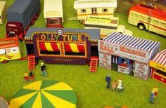 an assortment of toy vehicles and people in a miniature circus setting with tents, umbrellas and other toys