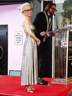 a woman in a silver dress standing at a podium with a man wearing a black suit and tie