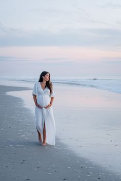 a pregnant woman standing on the beach at sunset