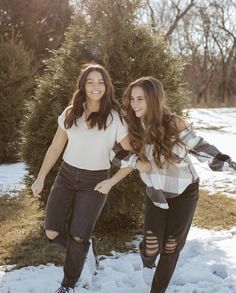 two young women standing next to each other in front of a snow covered field with trees