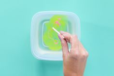 a hand holding a toothbrush in a plastic container on a blue surface with green and pink designs