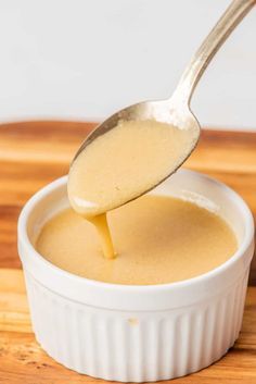 a spoon is pouring sauce into a small white bowl on a wooden table with a wood cutting board