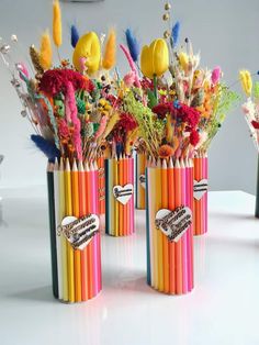 three pencils with flowers in them sitting on a table next to some other colored pencils