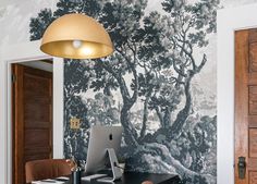 a desk with a laptop on it in front of a wallpapered tree mural