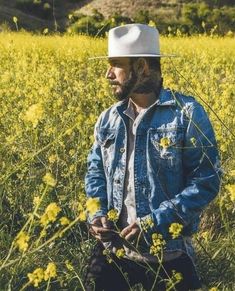 a man with a cowboy hat is sitting in the middle of a field full of yellow flowers