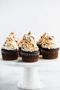 chocolate cupcakes topped with white frosting and sprinkles on a cake plate