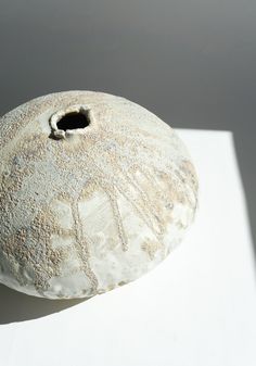 a white vase sitting on top of a table next to a shadow from the wall