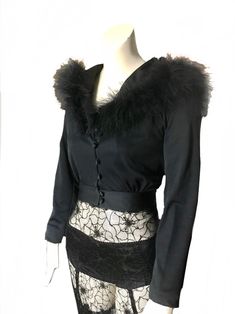 "a  vintage 1970s black hooded feather cropped jacket this stylish evening jacket is made of jersey blend fabric with stretch. this short jacket /top has small fabric covered buttons down the front, long sleeves, fitted waist. it has a beautiful dramatic hood that is adorned with fluffy black feathers around the rim not lined. the jacket is perfect for your Halloween gothic Victorian style party, it can also be worn as a top/blouse. the jacket is Mint Pristine vintage condition, no flaws to ment Long Sleeve Tops With Feather Trim For Evening, Fitted Black Outerwear With Feather Trim, Long Sleeve Feathered Tops For Fall, Long Sleeve Tops With Feather Trim For Fall, Long Sleeve Feather Top For Fall, Black Feathered Party Top, Winter Party Tops With Feather Trim, Winter Party Top With Feather Trim, Vintage Fitted Cropped Jacket For Winter