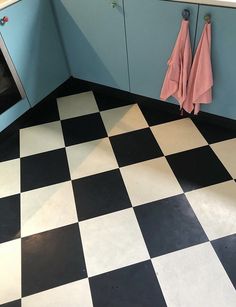 a black and white checkered floor in a kitchen next to cabinets with pink towels hanging on them