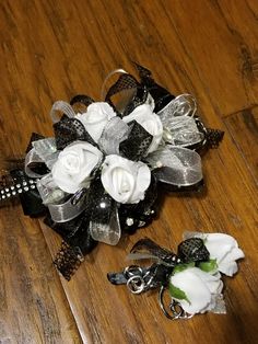 a bridal corsage with white roses and black ribbons on a wooden floor