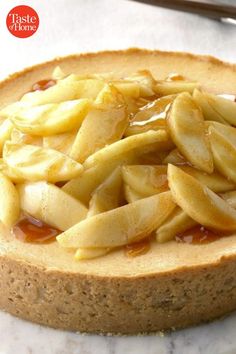 a cheesecake with apple topping on a marble platter next to silverware and utensils