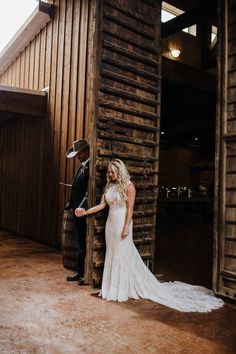 a bride and groom standing in front of an old wooden building holding each other's hand