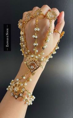 a woman's hand wearing a gold and white beaded bracelet with pearls on it