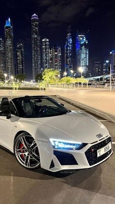 a white sports car parked in front of a cityscape with skyscrapers at night