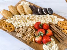 a wooden platter filled with cookies, crackers, strawberries and pretzels