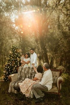 a family sitting on a couch in the woods with christmas tree and lights behind them