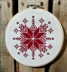 a red and white cross stitched snowflake is hanging on a wooden fence