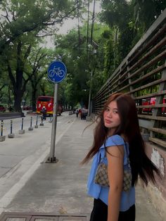 a woman with long hair standing next to a blue sign on the side of a road