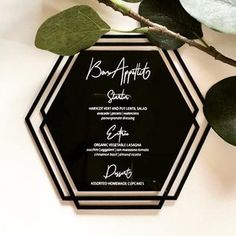 a black and white hexagonal shaped menu on a table with green leafy branches