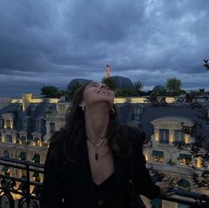 a woman looking up at the sky while standing on a balcony with buildings in the background