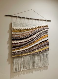 a wall hanging made out of different colored yarns on a white wall with a metal bar