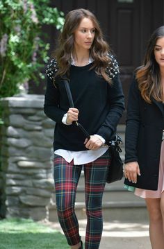 a woman in plaid pants and black sweater walking down the street with her hand on her hip