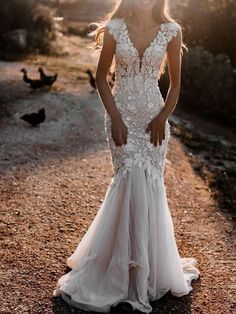 a woman in a white wedding dress standing on a dirt road with ducks behind her