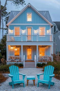 two lawn chairs sitting in front of a blue house at night with lights on the windows