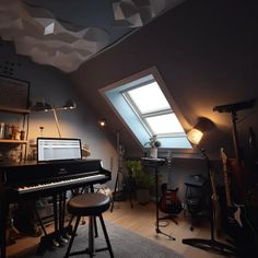 a room with a piano, stools and other musical instruments in the corner under a slanted skylight