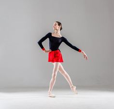 a young ballerina in red and black is posing for the camera with her hands behind her back