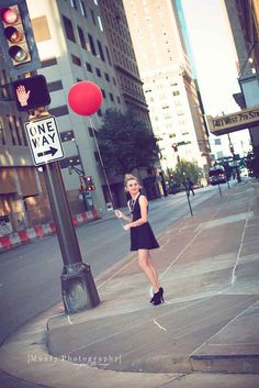 a woman standing on the side of a street holding onto a red balloon with one way sign above her head