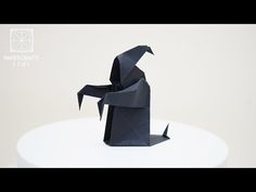 a black origami bird sitting on top of a white table next to a wall