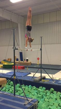 a person on a balance beam in an indoor gymnastics gym with green foams all over the floor