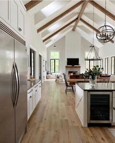 an open kitchen with white cabinets and wood flooring is pictured in this image, there are two chandeliers hanging from the ceiling