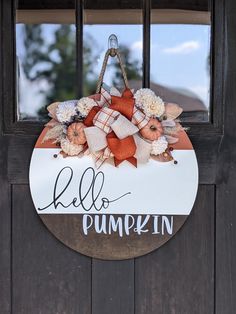 a wooden door with a hello pumpkin sign hanging from it's side and flowers in the center