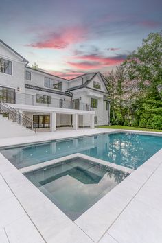 an empty swimming pool in front of a large white house with trees on the other side