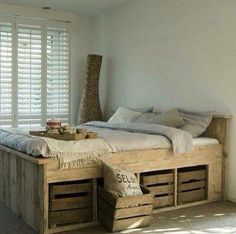 a bed made out of wooden crates with pillows and blankets on it, in a room with white walls