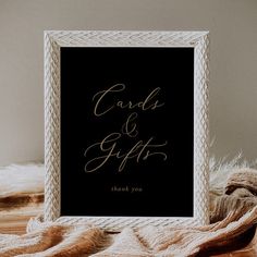 a black and gold wedding card and gift sign on a table next to a pile of blankets