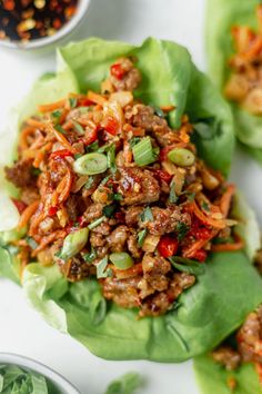 lettuce wraps filled with meat and vegetables on a white surface next to small bowls